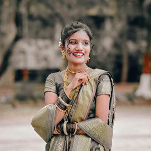 A joyful woman in a traditional Maharashtrian sari and jewelry, smiling outdoors in Nashik, India.